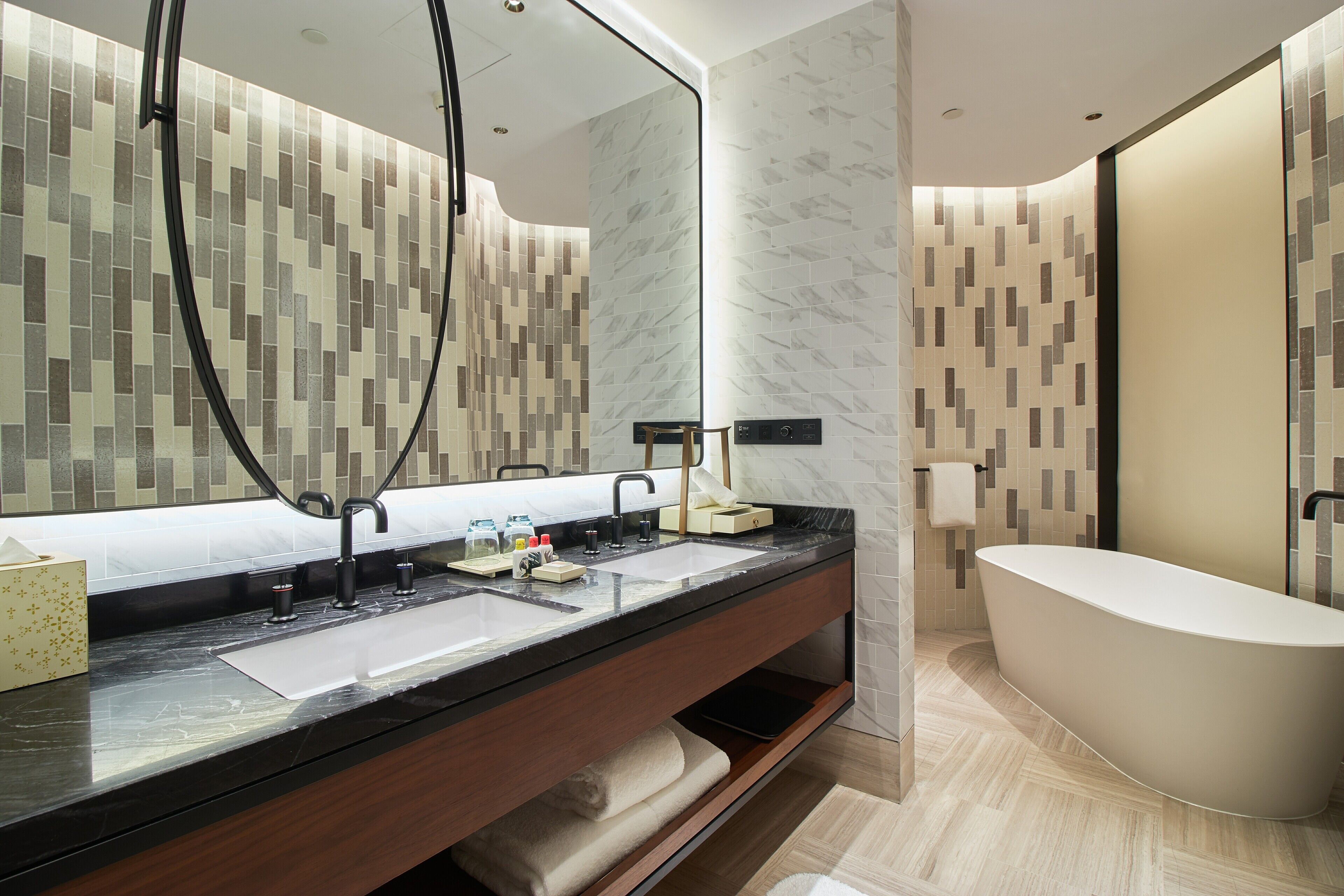 A modern bathroom with a large mirror, two sinks, a bathtub, and a vanity with storage.