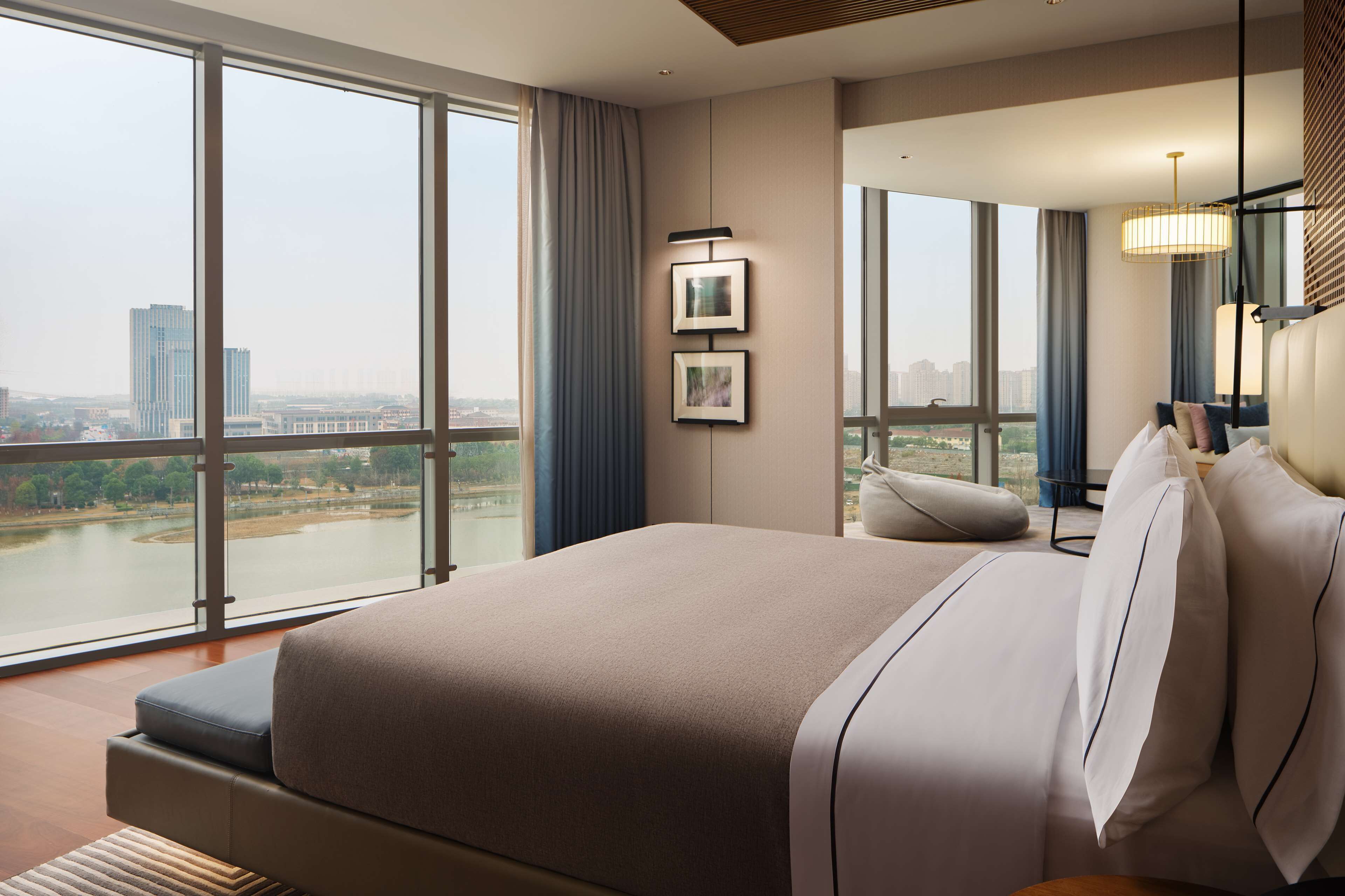 A modern hotel room with a large bed, a view of a cityscape, and a city park visible through the window.