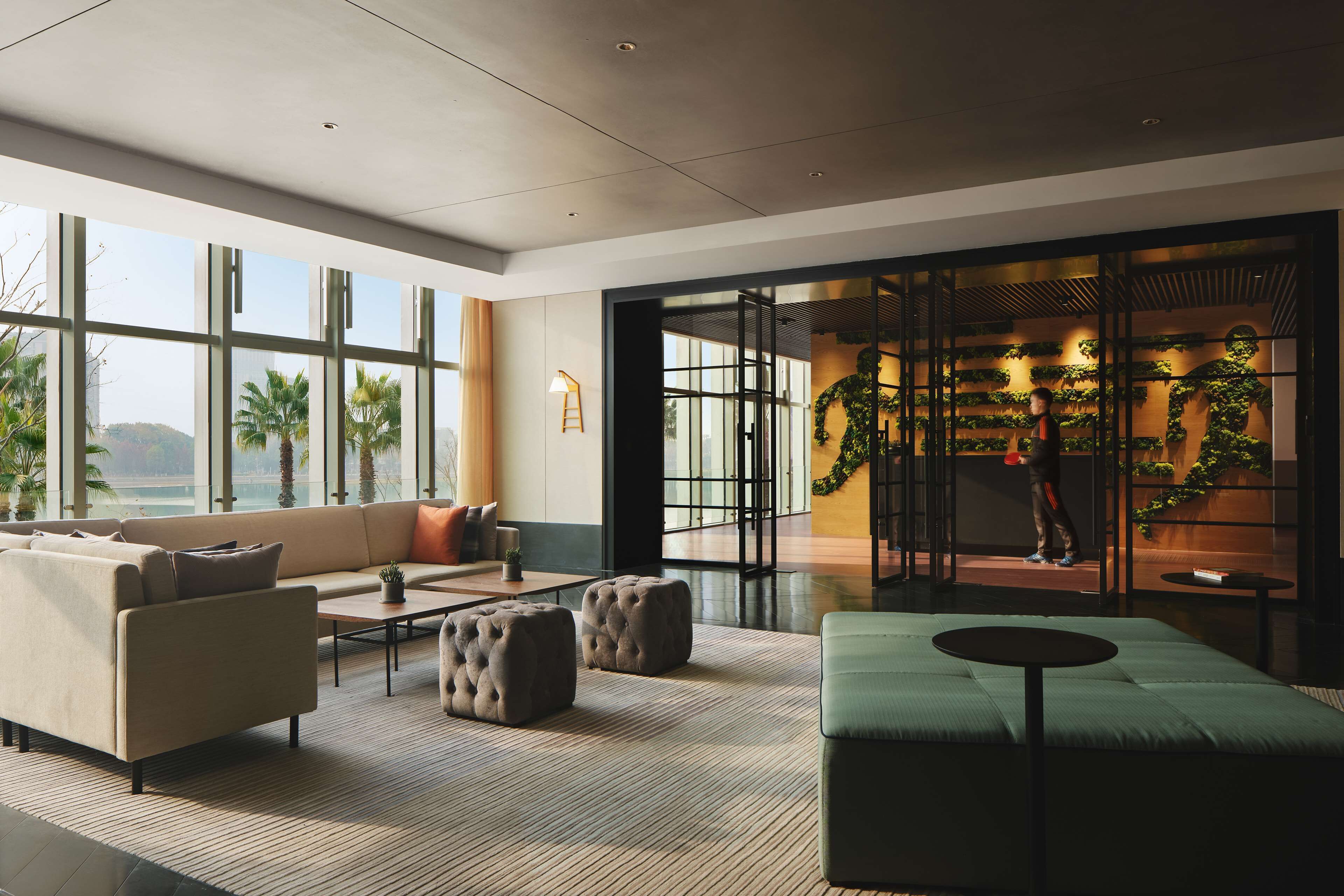 A modern hotel lobby with a large sofa, ottomans, a coffee table, and a view of the outdoors through large windows.