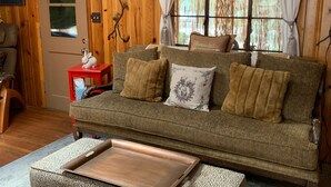 Una sala de estar acogedora con un muro de madera, un sofá con cojines, una mesa de centro y un ventilador de techo.