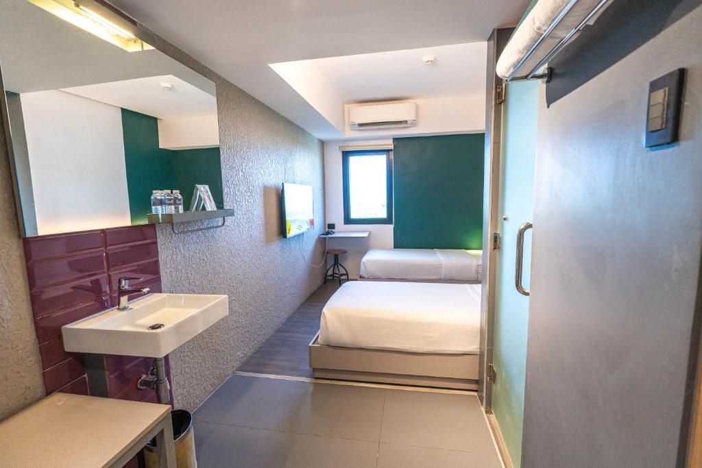 Quarto de hotel com cama, pia, espelho e janela.