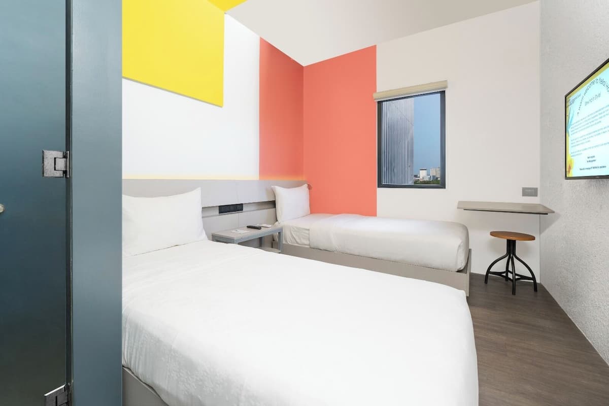 Quarto de hotel com duas camas, uma mesa pequena e uma janela.