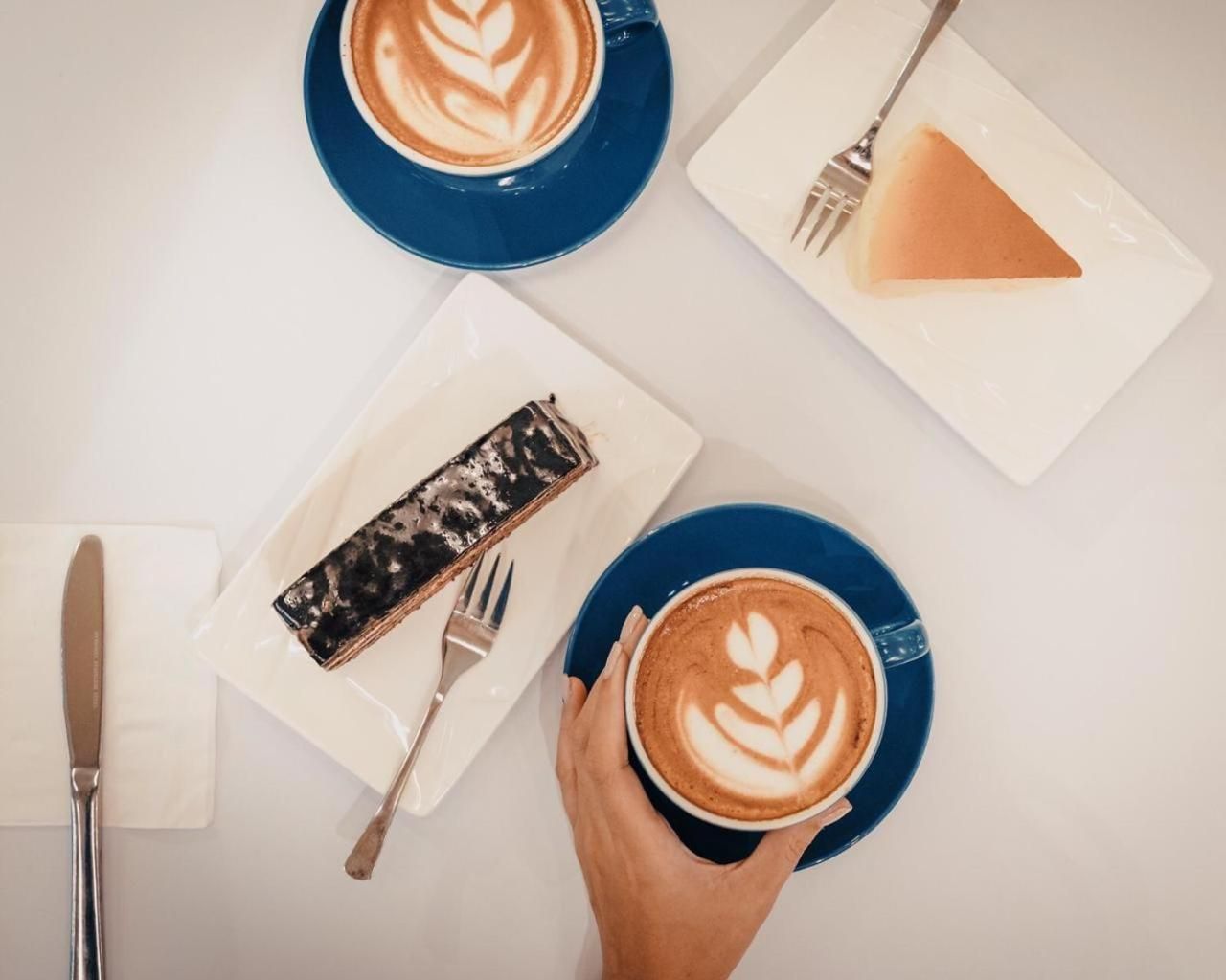 Une table avec deux tasses de café, une part de gâteau et un dessert sur une assiette, ainsi que des couverts.