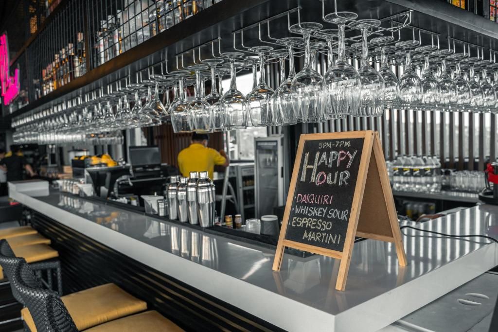 Zona de bar con un cartel de pizarra que enumera bebidas de la hora feliz y una fila de vasos colgantes.