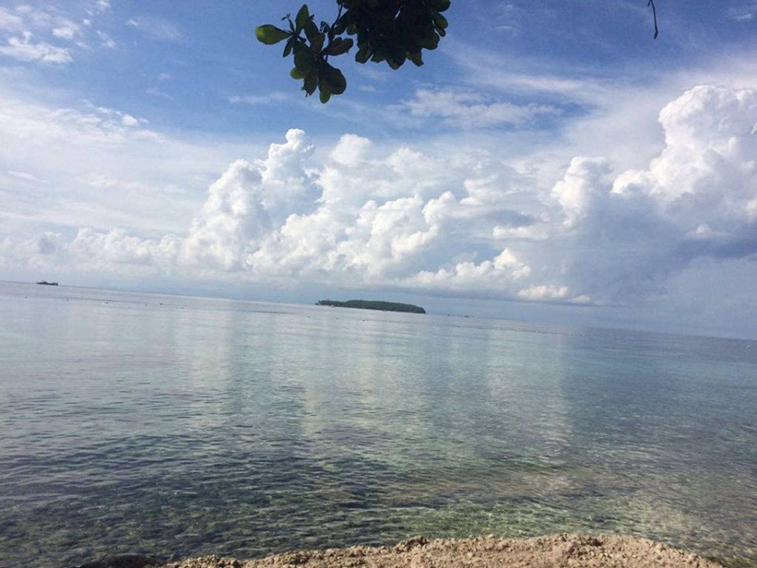 Una vista despejada de un mar tranquilo con una isla distante y un barco a lo lejos.