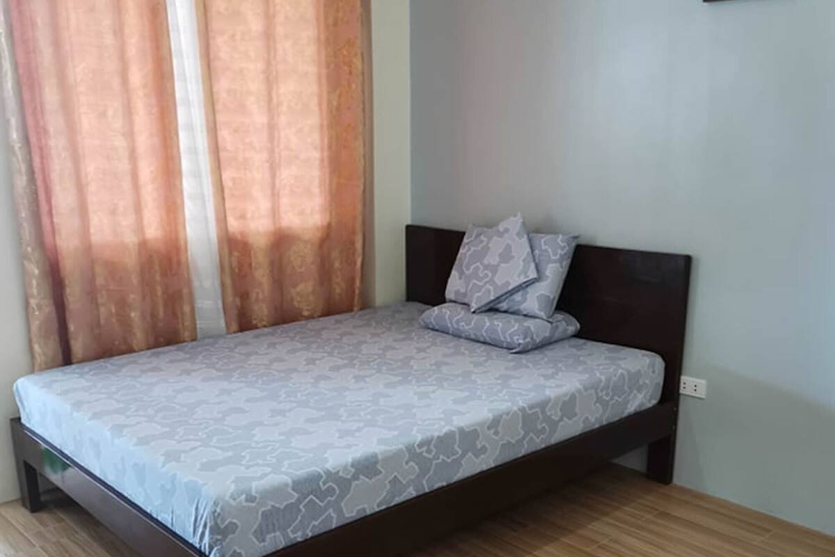 A bedroom with a bed, curtains, and a framed picture on the wall.