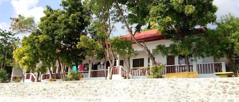 A building with a red roof and white walls, surrounded by trees and a sandy area.
