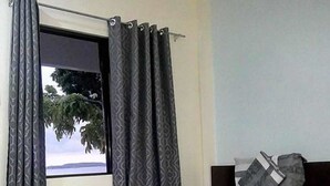 Un dormitorio con cama, cortinas y ventana con vista a árboles.