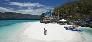 A beach with a white sand shore, a few people standing, and a blue boat near the water.