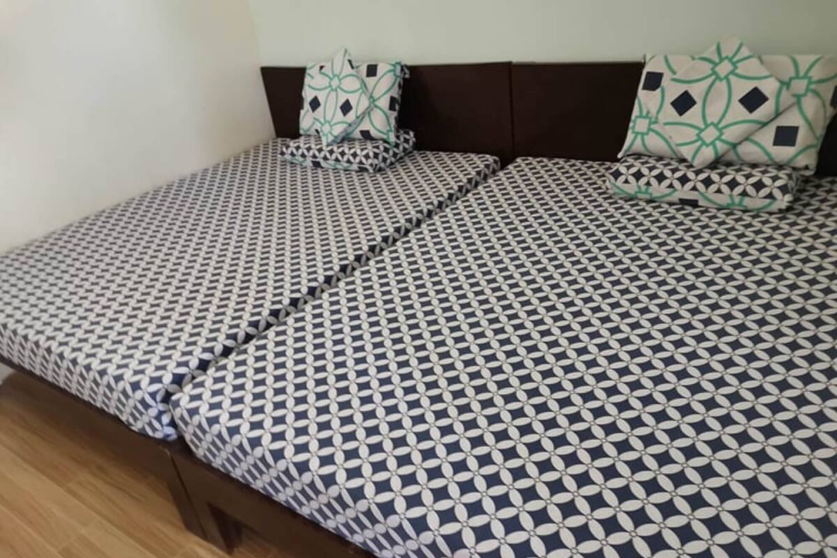 A bed with a geometric patterned bedspread and matching pillows, a wooden floor, and a dark headboard.