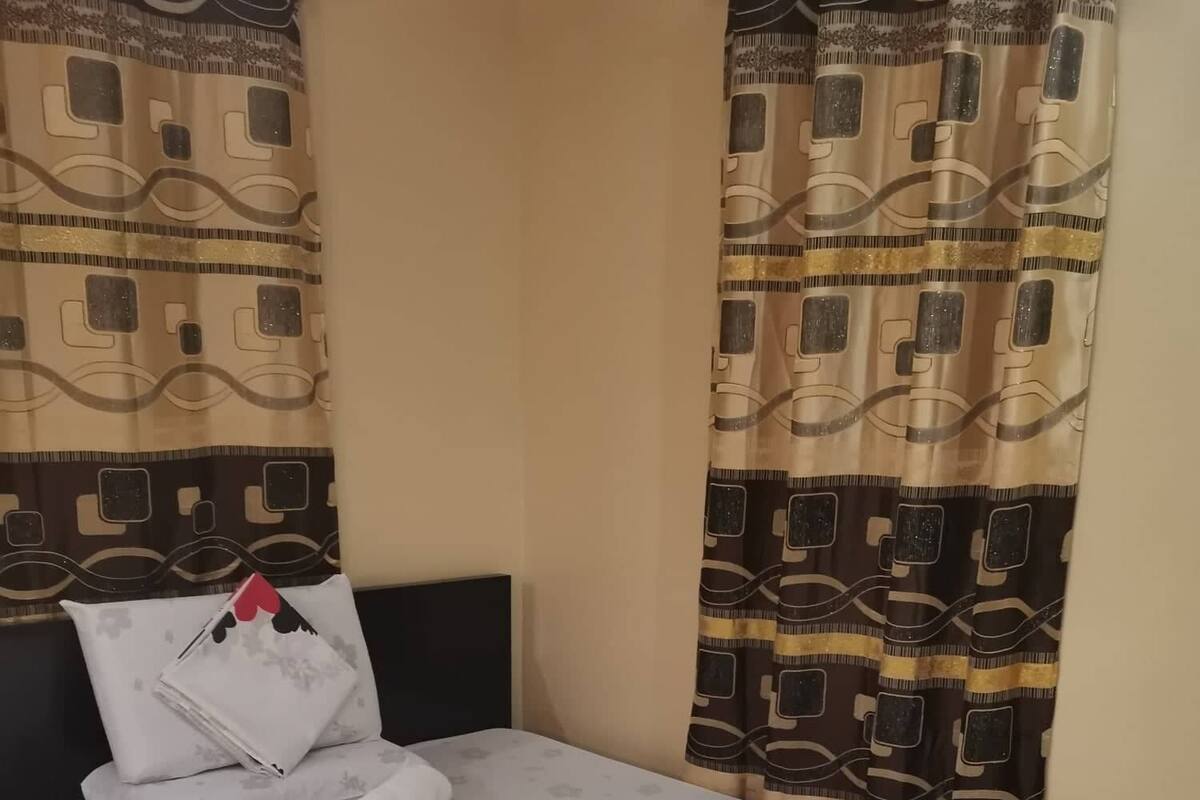 A neatly made bed with a floral-patterned bedspread, a pillow with a red heart, and a folded white towel.