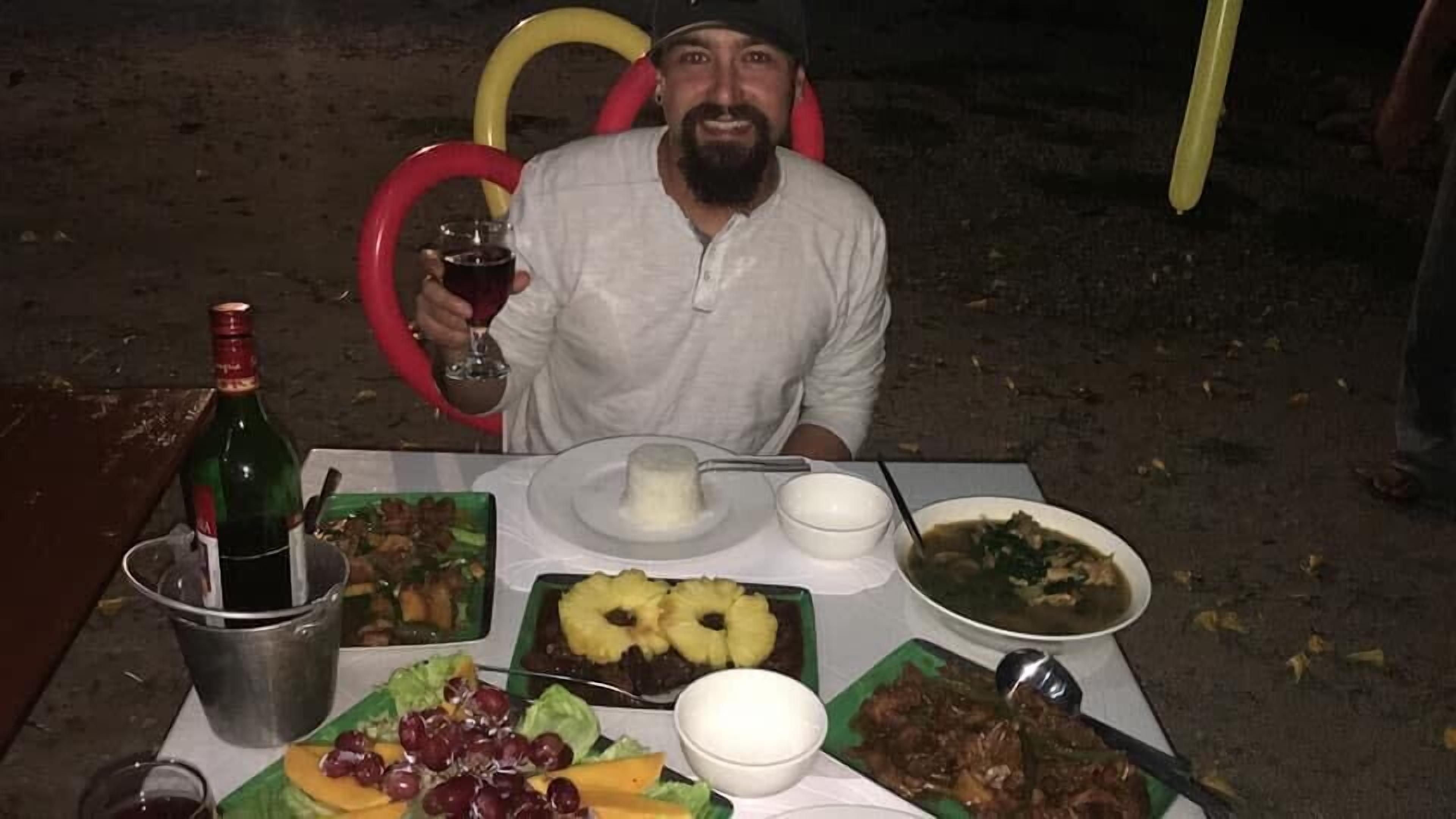 A table set outdoors with various dishes, a bottle of wine, and a glass.