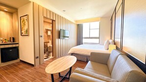A hotel room with a bed, a sofa, a TV, a small table, a desk with a coffee machine, and a bathroom visible through an open door. - Hotel A . Tainan (Tainan)