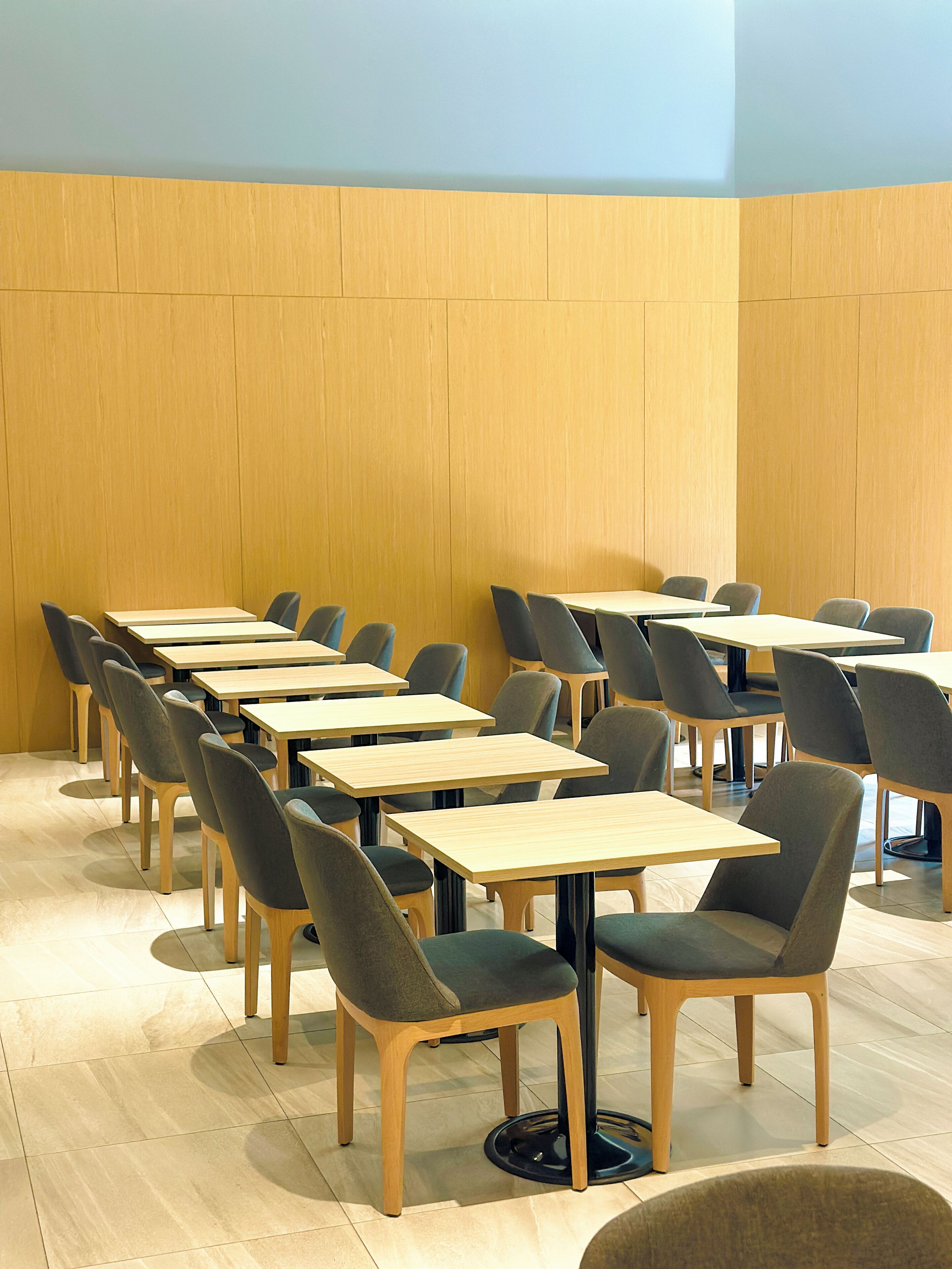 Een vergaderruimte met meerdere tafels en stoelen, houten paneelwanden en een betegelde vloer.