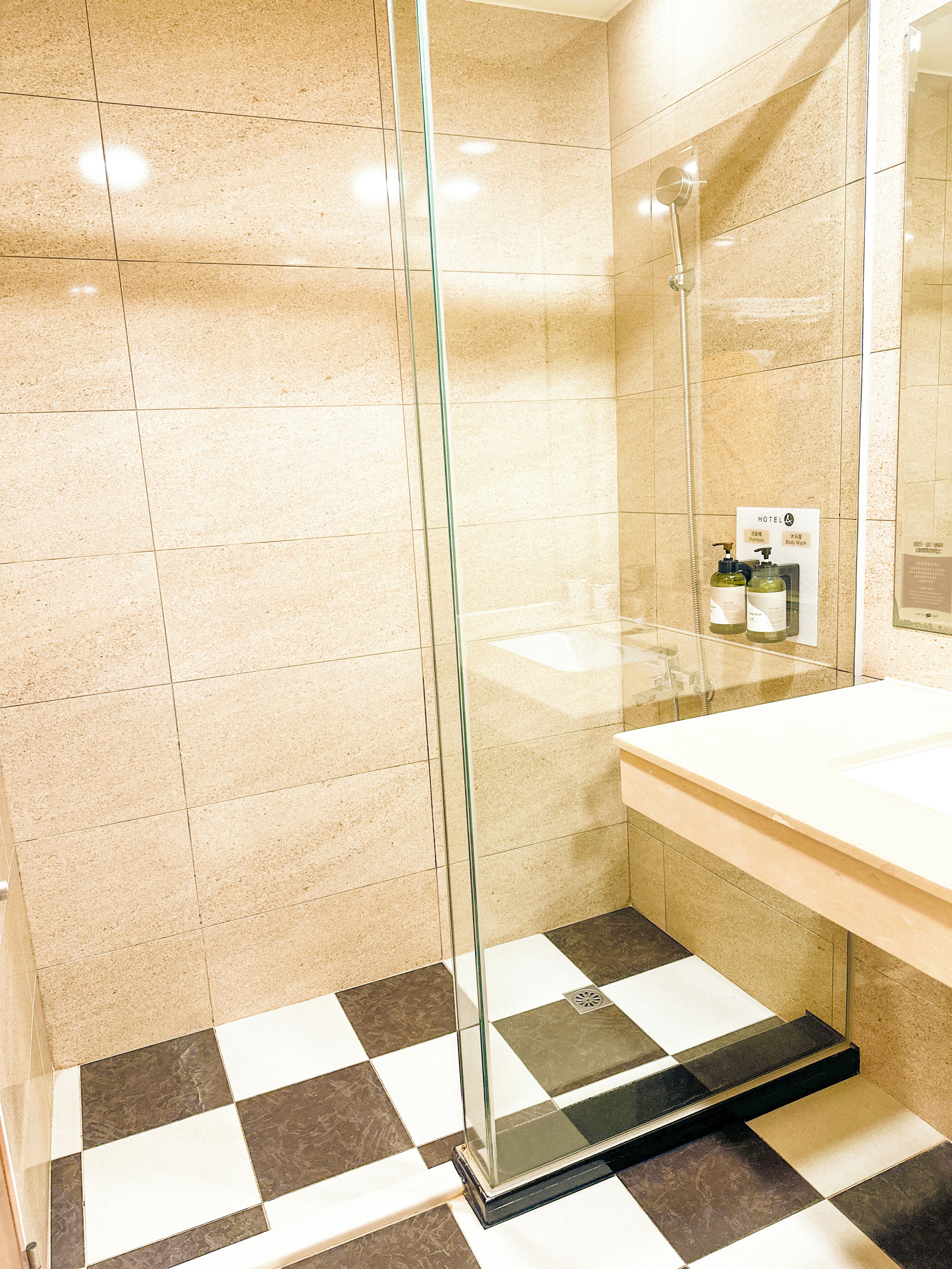 A hotel bathroom with a glass-enclosed shower, a white sink, and a checkered floor pattern.