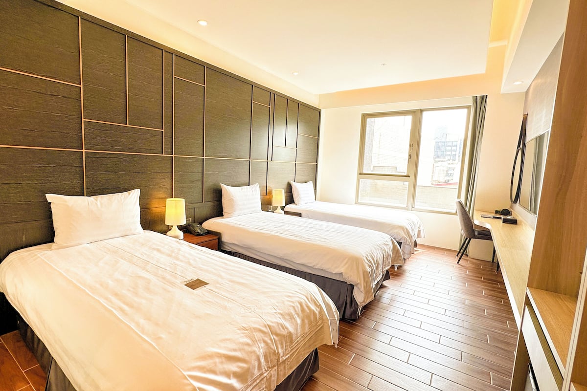 A hotel room with two beds, a wooden headboard, a large window, and a TV.