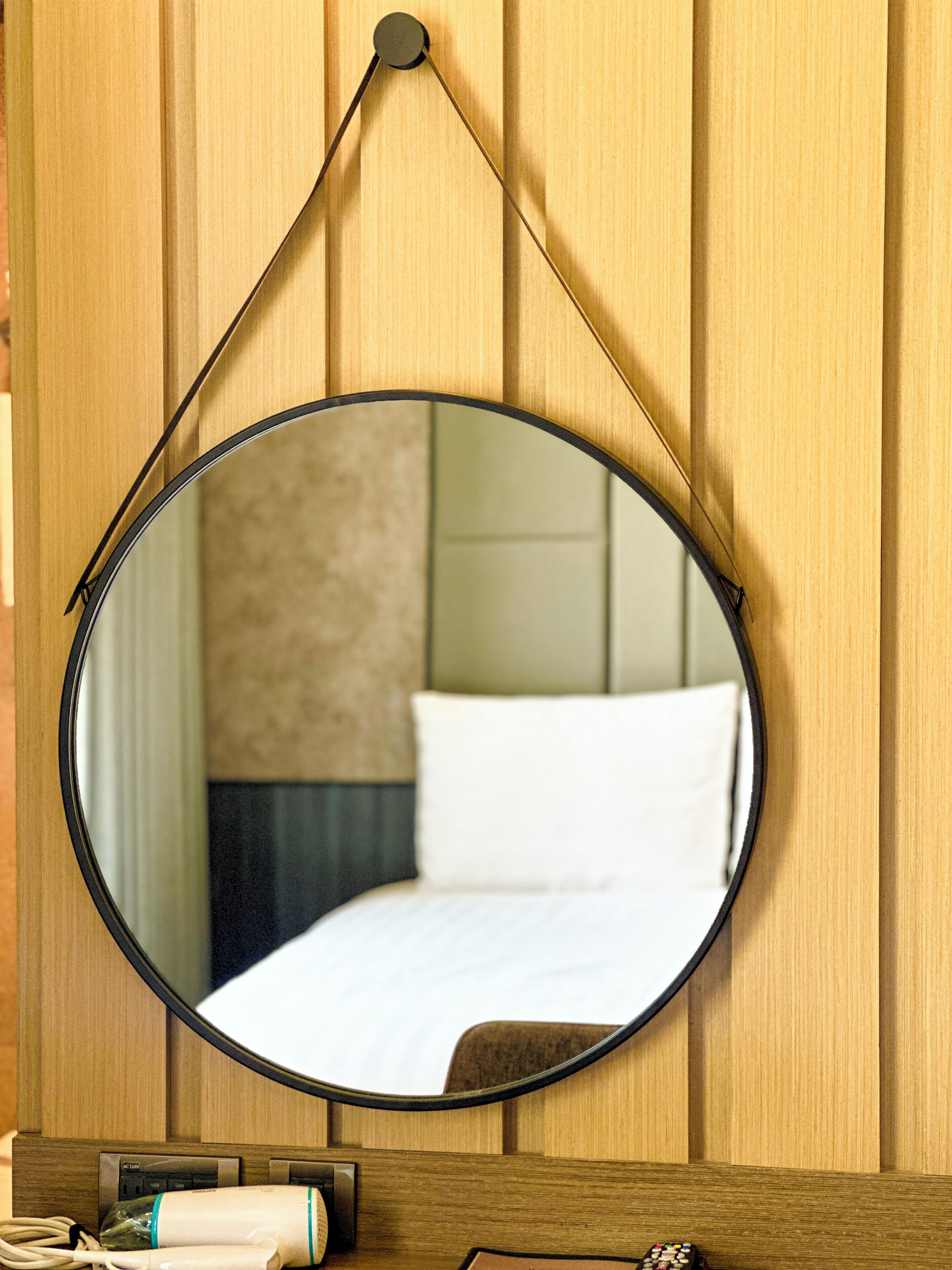 A round mirror with a black frame, mounted on a wooden wall.