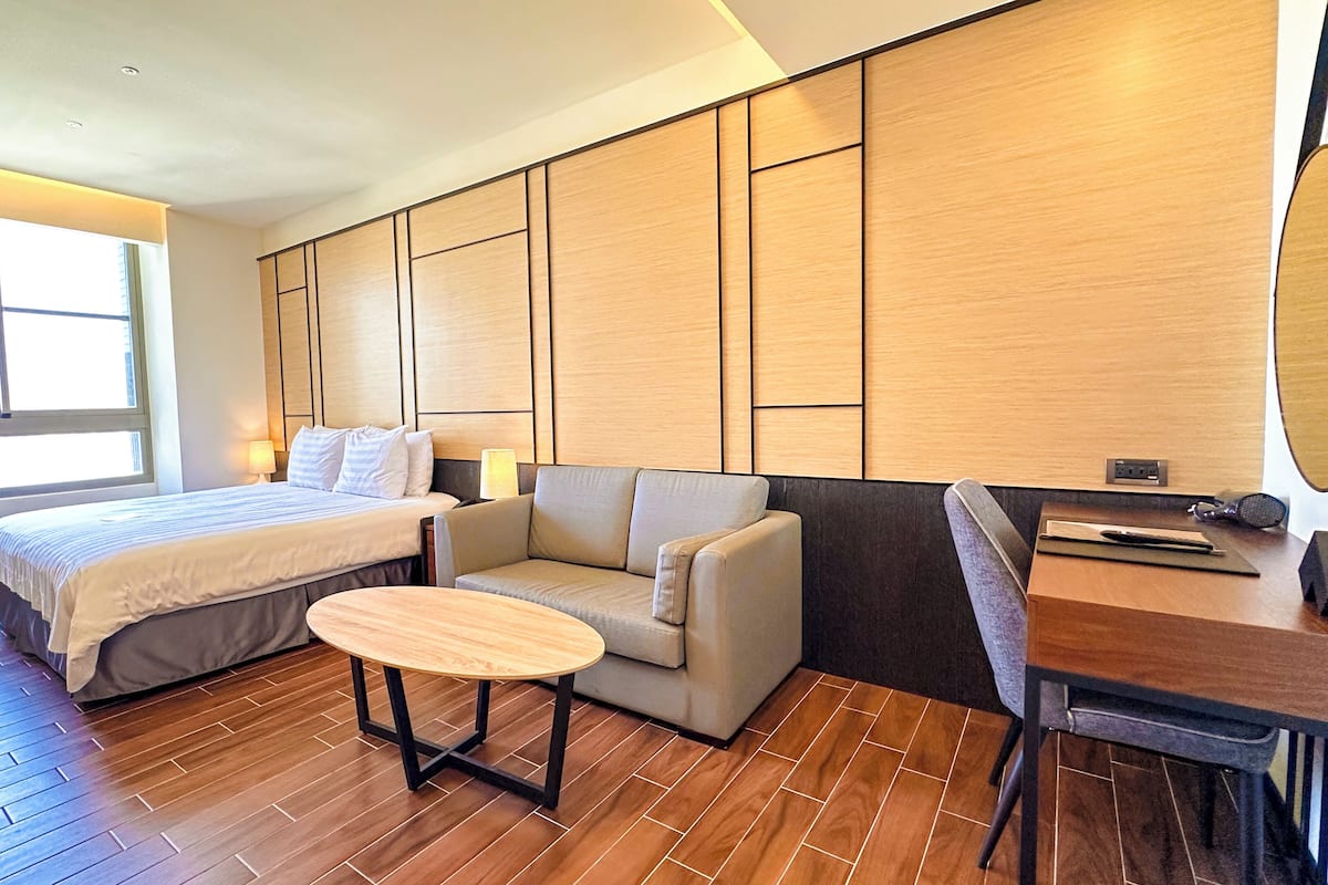 A hotel room with a bed, a sofa, a small table, and a desk with a chair.