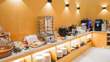 Montaje de bufé con diversos alimentos, una máquina de café y dispensador de bebidas.