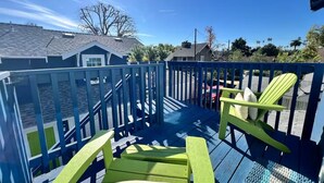 Um deck azul com uma cadeira verde e um encosto, céu claro e uma casa ao fundo.