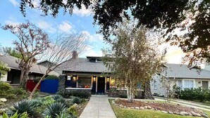Uma casa residencial com fachada de pedra, varanda frontal e um jardim bem cuidado com diversas plantas.
