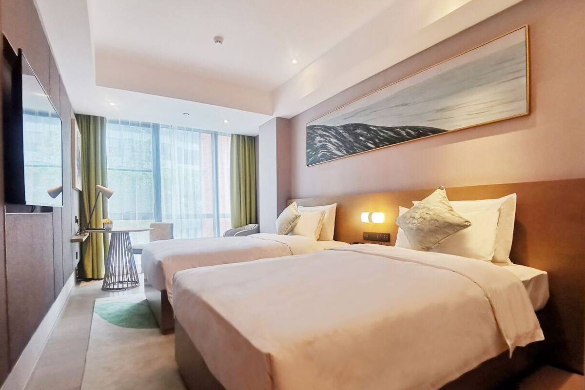 Ein Hotelzimmer mit zwei Betten, einem Schreibtisch und einem großen Fenster mit Vorhängen.