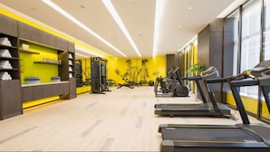 Une salle de sport moderne équipée de tapis de course, d’appareils de musculation et d’un mur jaune vif.