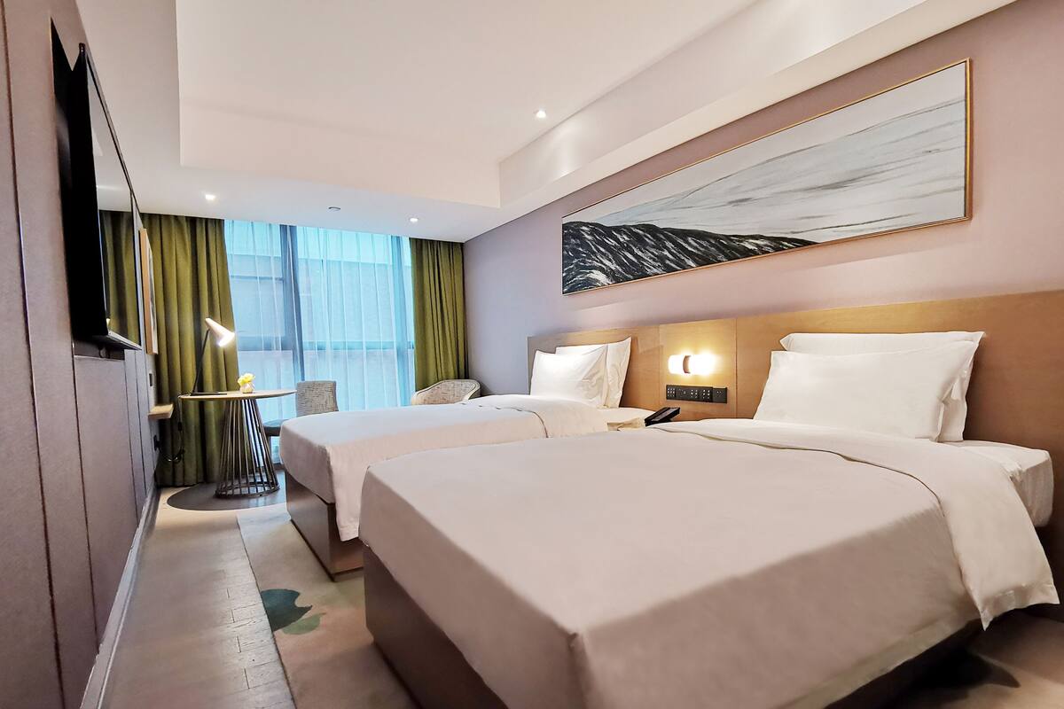 Ein Hotelzimmer mit zwei Betten, einem Schreibtisch, einem Sessel, einem Fernseher und einem Bild an der Wand.