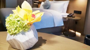 Une chambre d’hôtel avec un lit, une table de chevet, une lampe et un vase rempli de fleurs.
