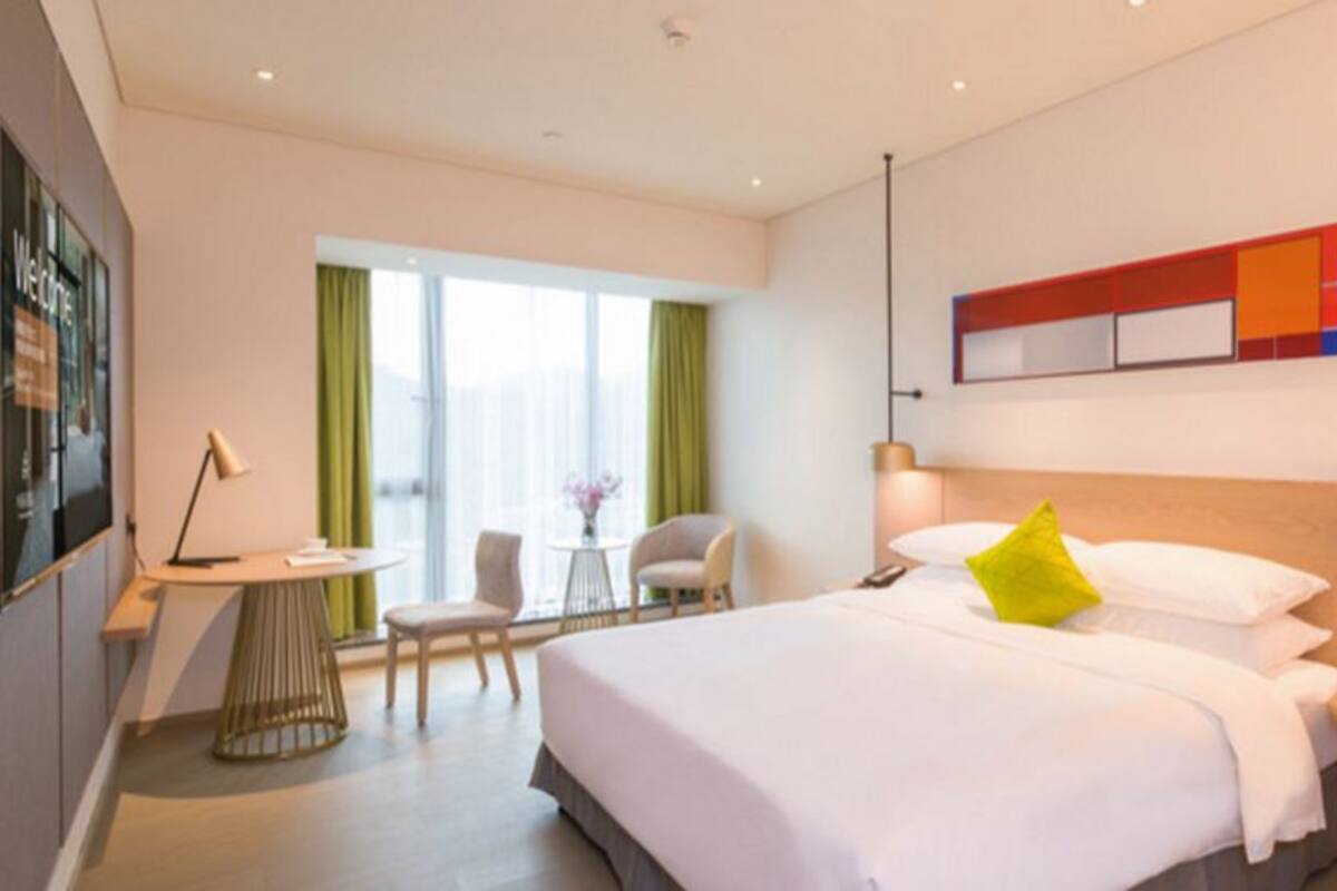 Ein modernes Hotelzimmer mit einem großen Bett, einem Schreibtisch, einem Stuhl und einem fenster mit Vorhängen.