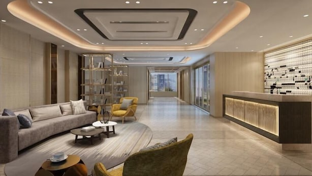 Un hall d’hôtel moderne avec un canapé, des fauteuils, une table basse, une bibliothèque et un comptoir d’accueil.