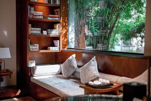 Un rincón acogedor para leer con un banco acolchado, una estantería de madera y una ventana con vistas a la vegetación.