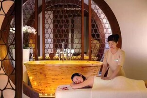 Um quarto de spa com uma banheira de madeira, mesa de massagem e um painel decorativo de madeira.