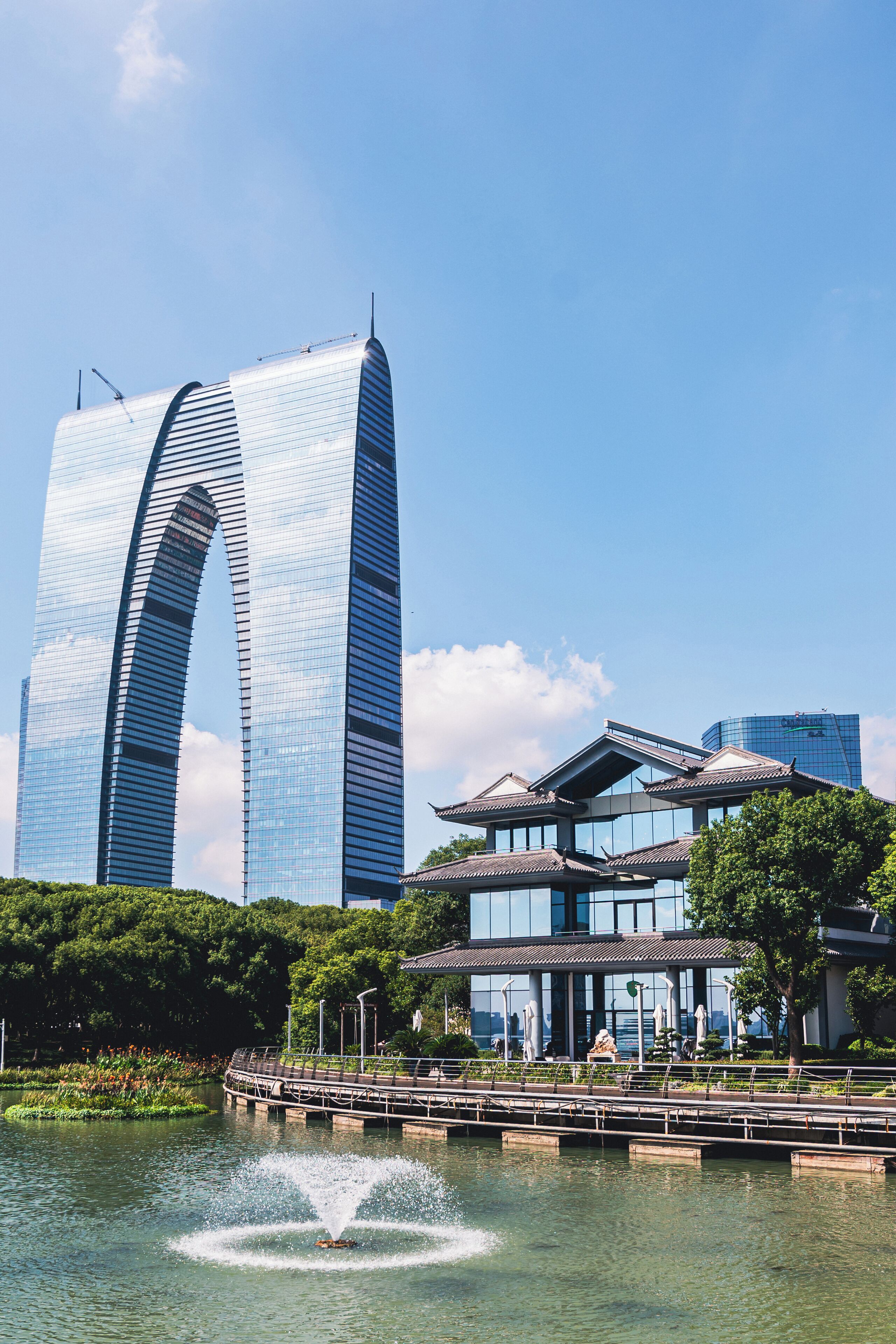 A modern building with a unique curved design, a traditional building with a tiled roof, and a water fountain in the foreground.