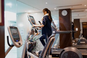 Een vrouw die op een loopband traint in een sportschool met glazen wanden en een klok aan de muur.