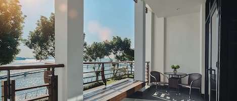 A balcony with a view of a river, a table with chairs, and a railing.