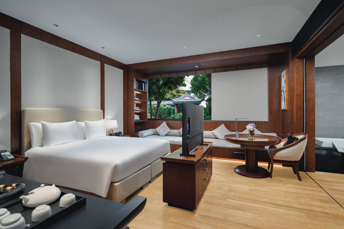 Une chambre d’hôtel moderne dotée d’un grand lit, d’une télévision, d’une table à manger et offrant une vue sur un bâtiment traditionnel.