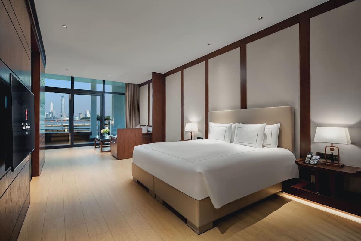 Une chambre d’hôtel moderne dotée d’un grand lit, d’une télévision, d’un bureau et offrant une vue sur le panorama urbain.