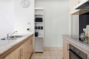 Una cocina con encimeras de granito, un lavamanos doble, un armario blanco y un reloj en la pared.