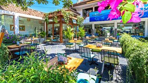 An outdoor café with wooden tables and chairs, surrounded by lush greenery and vibrant flowers. - Akaya Bali (Denpasar)