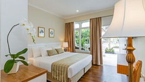 A hotel room with a bed, a nightstand, a lamp, a window with curtains, and a view of the outdoors. - Akaya Bali (Denpasar)
