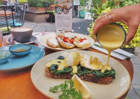 Una mesa con alimentos para el desayuno, incluyendo huevos benedictinos, panqueques y una taza de café.