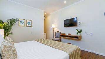 A hotel room with a bed, a chair, a TV, a lamp, and framed pictures on the wall.