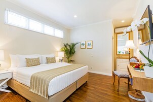 Habitación de hotel con una cama grande, un escritorio con lámpara, una silla y una mesita con planta.