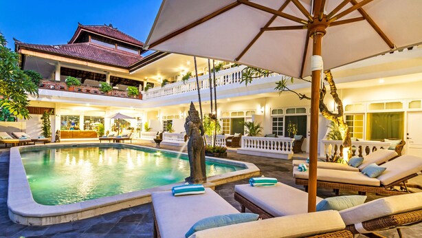 A pool area with lounge chairs and umbrellas, a statue, and a building with balconies and plants. - Akaya Bali (Denpasar)