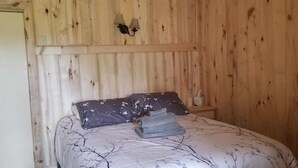A bedroom with a wooden wall, a bed with floral bedding, and a nightstand with a lamp. - Sweet Seclusion Cabin with Shower (Healy)