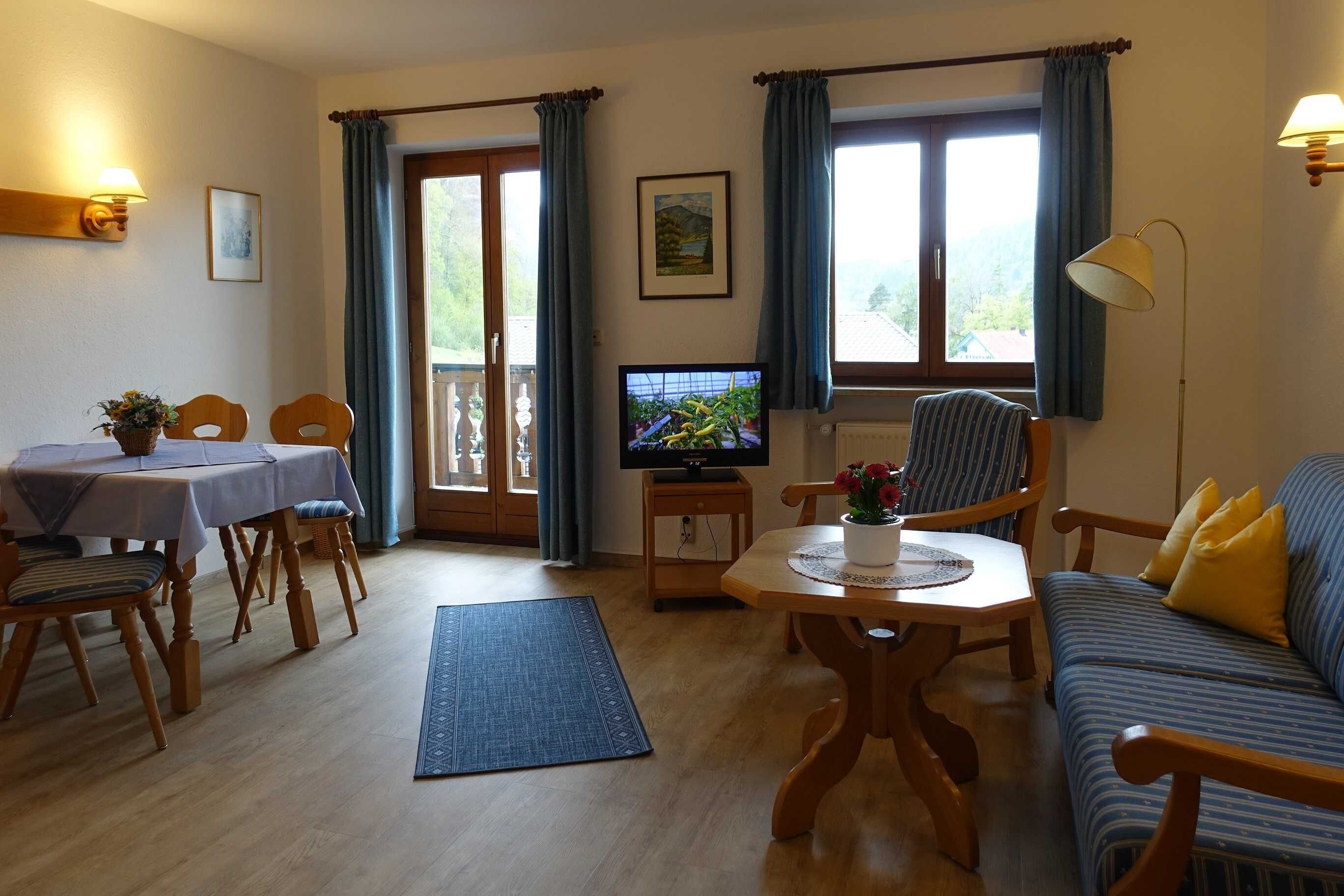 Una sala de estar con una mesa de comedor, sofá, televisor y vistas al exterior.