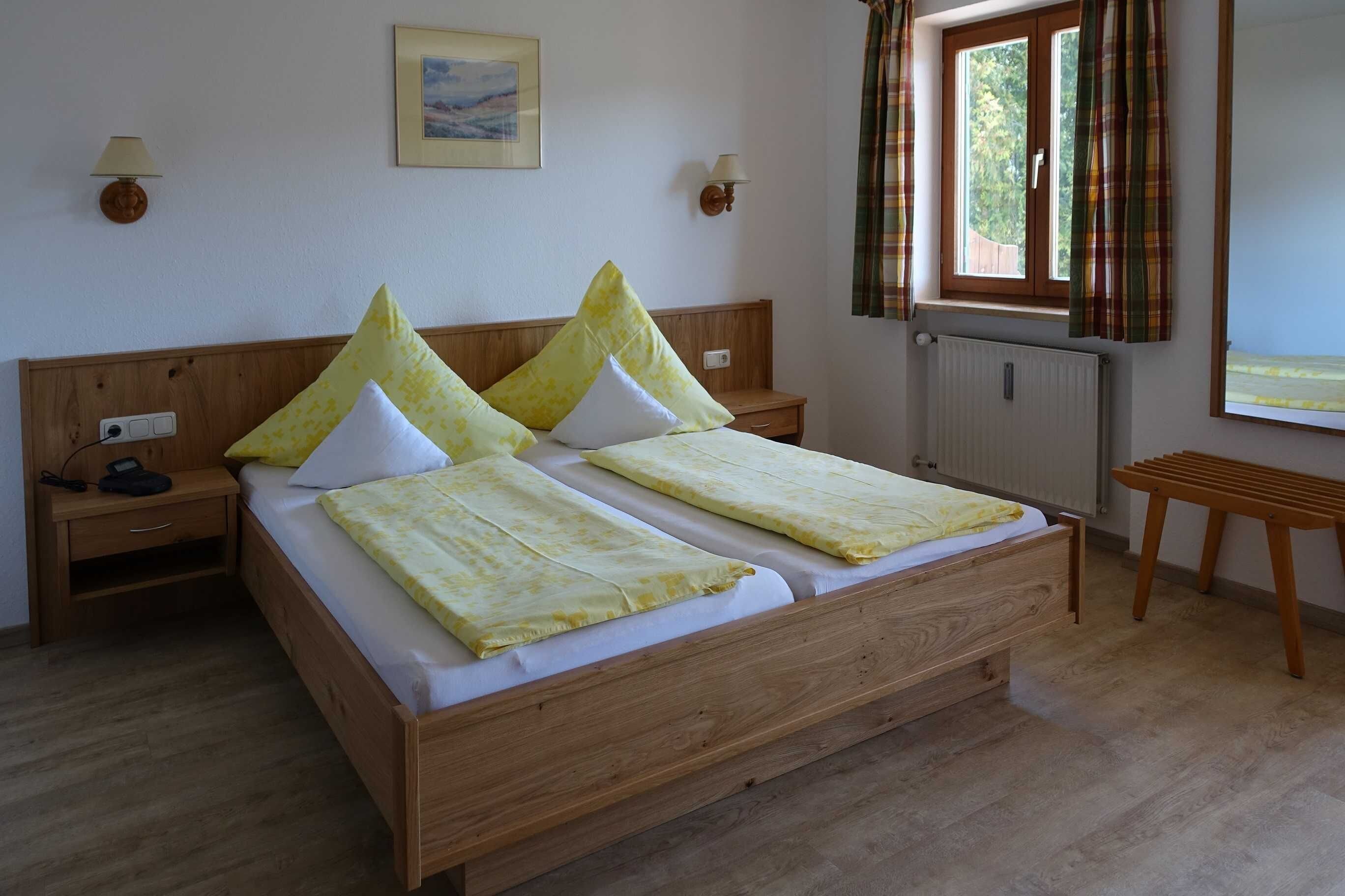 Una cama doble con cabecera de madera, dos mesitas de noche con lámparas, una ventana con cortinas y un radiador.