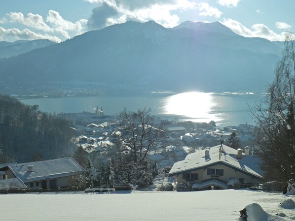A snow-covered landscape with a lake, mountains, and houses.