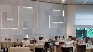 Un restaurant doté de nombreuses tables, chacune agrémentée de verres à vin et de couverts, et présentant un intérieur moderne avec des motifs géométriques sur les murs et un éclairage encastré.